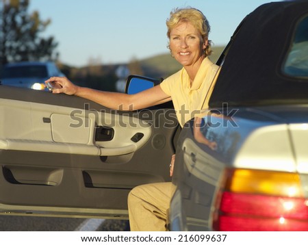 Mature woman with mobile phone in car, door open, portrait