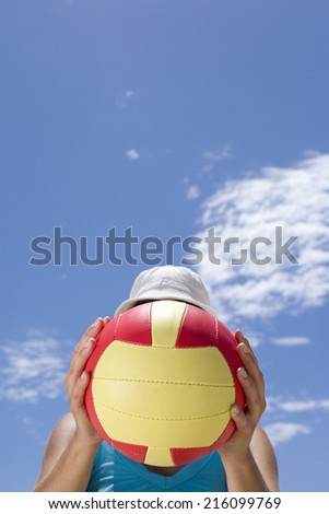 Girl obscuring face with ball outdoors, low angle view