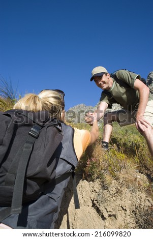 Young couple hiking, man helping woman up bank, low angle view