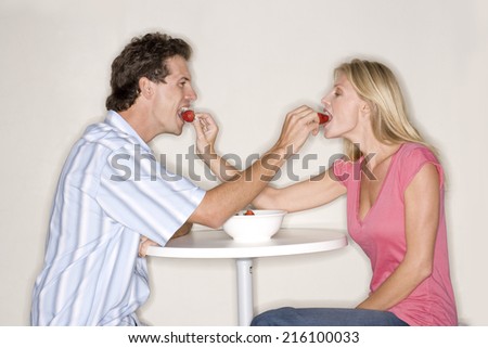 Young couple at table feeding each other strawberries, side view