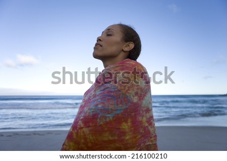 Young woman wrapped in sarong on beach, eyes closed, low angle view