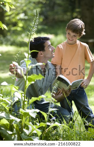 Father and son (8-10) looking at plants with nature book in forest