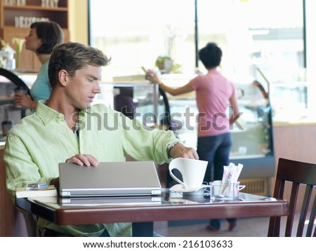 Young man with laptop computer in cafe, looking at watch