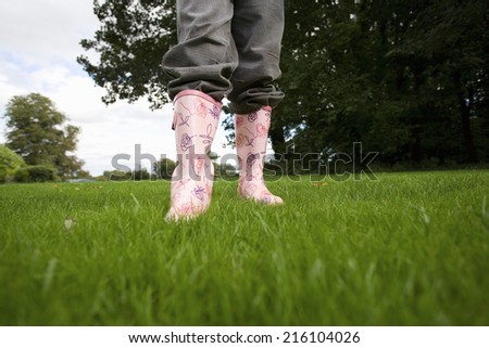Girl (8-10) in wellington boots on grass, low section