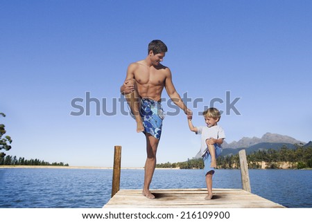Father and son balancing in lake dock