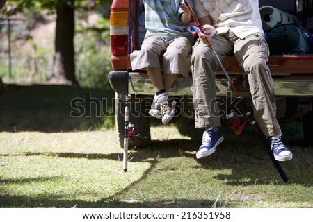 Father and son sitting with fishing poles on edge of truck bed