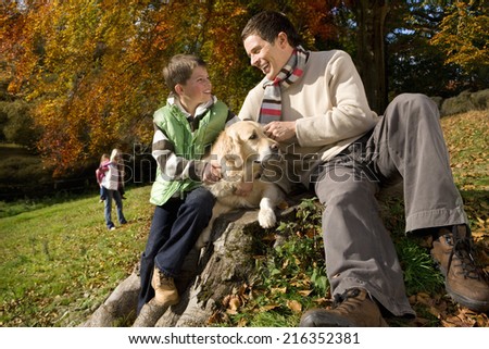 Father, son, and dog sitting on tree stump in woods