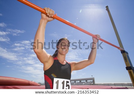 Young female athlete with hands on bar, low angle view (lens flare)