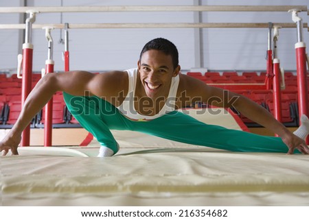 Male gymnast stretching in gymnasium, smiling, portrait
