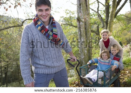 Portrait of man pulling children and wife in wheelbarrow