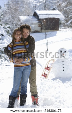 Portrait of mixed race couple standing in snow with snowman