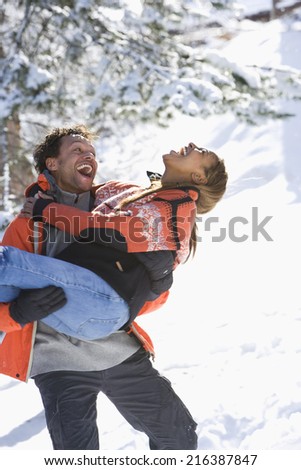 Playful mixed race couple in snow, man carrying woman