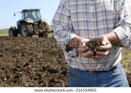 Close up of farmer cupping soil in ploughed field with tractor in background