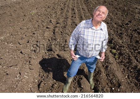 Farmer showing empty pockets and looking up in ploughed field