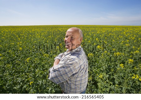 Smiling farmer standing with arms crossed in rape seed field