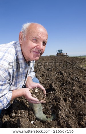 Farmer cupping soil with tractor and plough in background