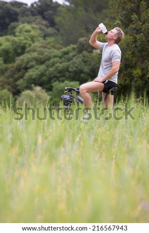 Man on bicycle drinking from water bottle in rural field