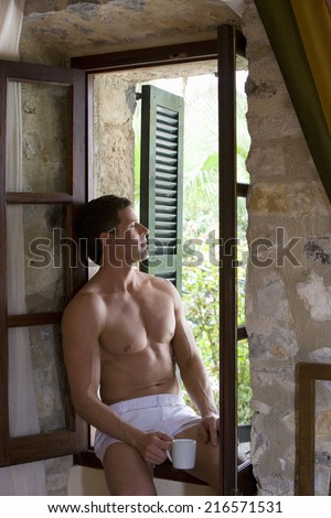 Man in boxer shorts drinking coffee on window ledge