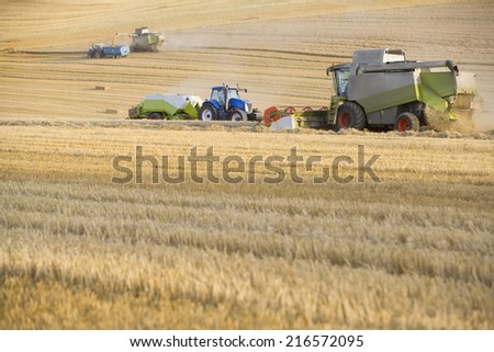 Combine harvesting wheat and straw baler in field