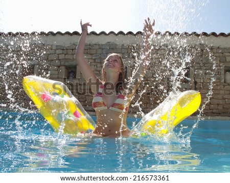 Teenage girl on pool raft splashing water in swimming pool