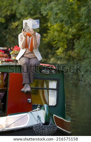 Woman reading book on narrow boat in canal