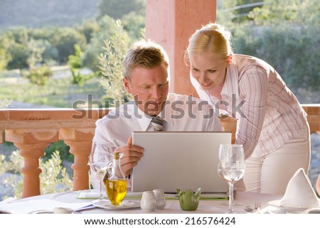 Businessman and businesswoman using laptop on restaurant balcony