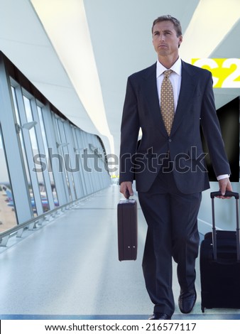 Businessman pulling rolling luggage in airport concourse