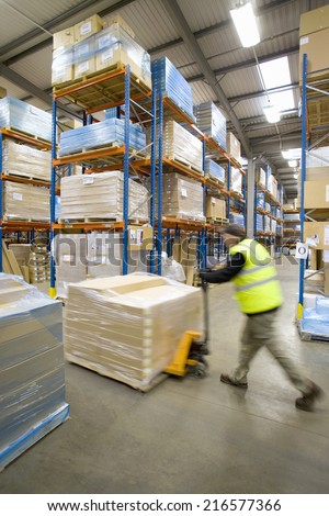 Warehouse worker pushing pallet truck with cardboard boxes