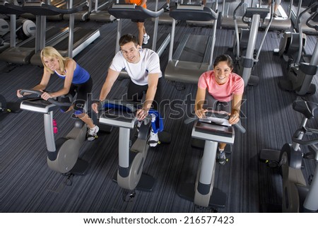 Portrait of man and women riding exercise bikes in health club