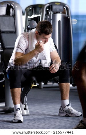 Man with towel resting on exercise equipment in health club