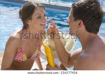 Man applying sunscreen to woman\'s nose at poolside