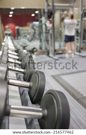 Rack of dumbbells in health club with man lifting weights in background