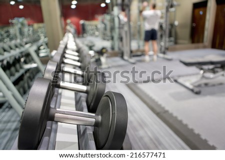 Rack of dumbbells in health club with man lifting weights in background