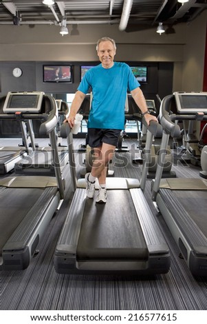 Portrait of smiling man standing on treadmill in health club