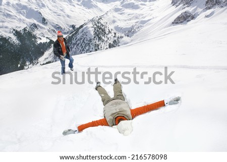 Man watching woman making snow angel on mountain
