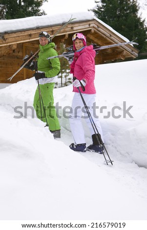 Couple standing in snow near lodge with skis