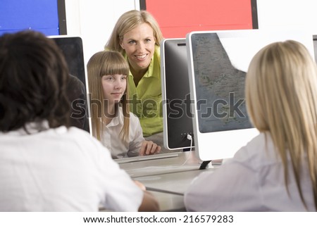 Teacher helping students working on computers in school computer lab