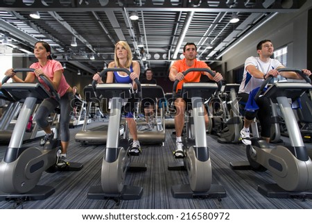 Men and women riding exercise bikes in health club