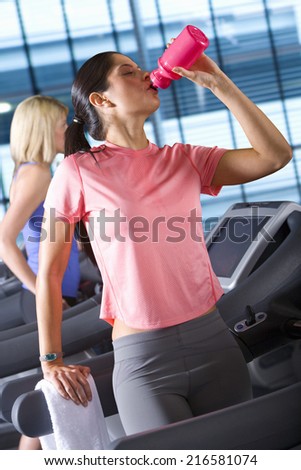 Woman drinking from water bottle on treadmill in health club