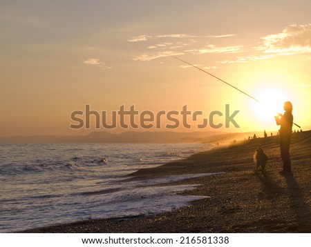 Silhouette of man fishing with fishing rod at ocean at sunset