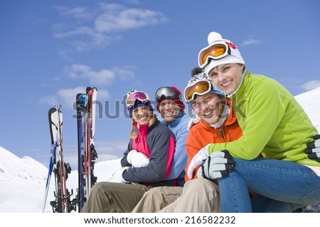 Smiling friends sitting with skis in snow