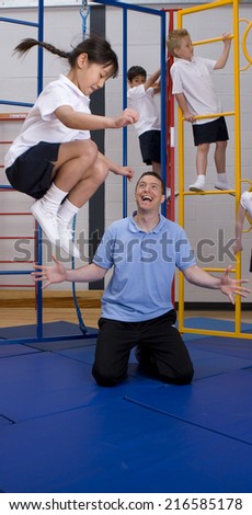 Gym teacher watching school girl jumping off climbing equipment