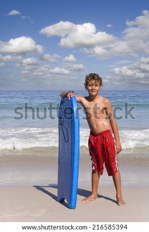 Boy standing on beach near ocean with body board