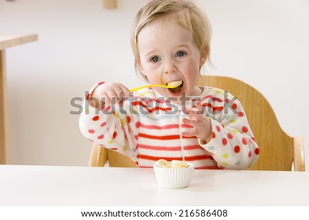 Baby girl in high chair eating banana slices