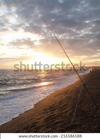 Tranquil sun setting on horizon over ocean with fishing rod in foreground
