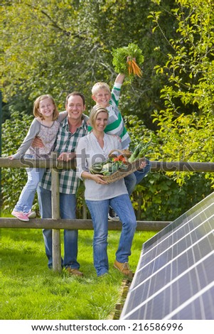 Happy family standing near solar panel holding garden vegetables