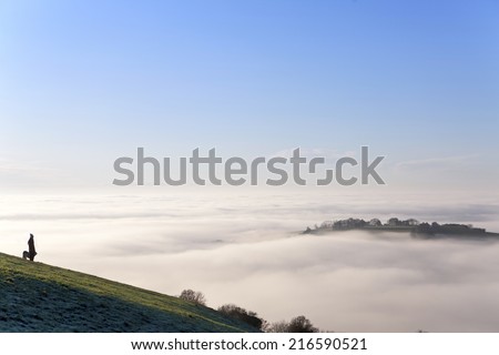 Dog and person standing on hill over fog covered valley
