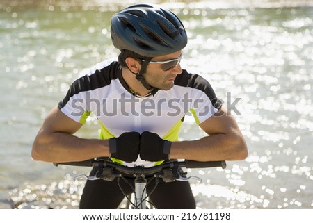 A man sitting on his cycle, river in background