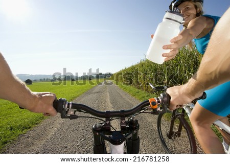 A woman giving her friend a bottle of water while cycling.