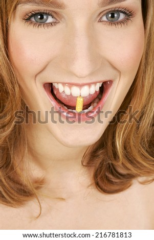 A woman holding a capsule between her teeth